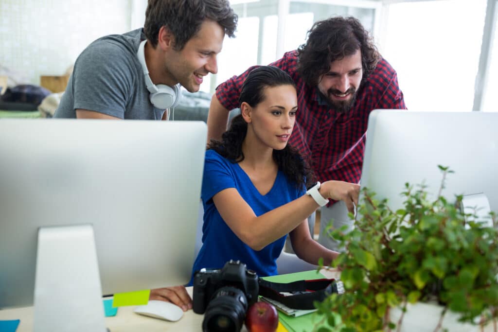 Drei Personen arbeiten gemeinsam als Mediengestalter am Computer.