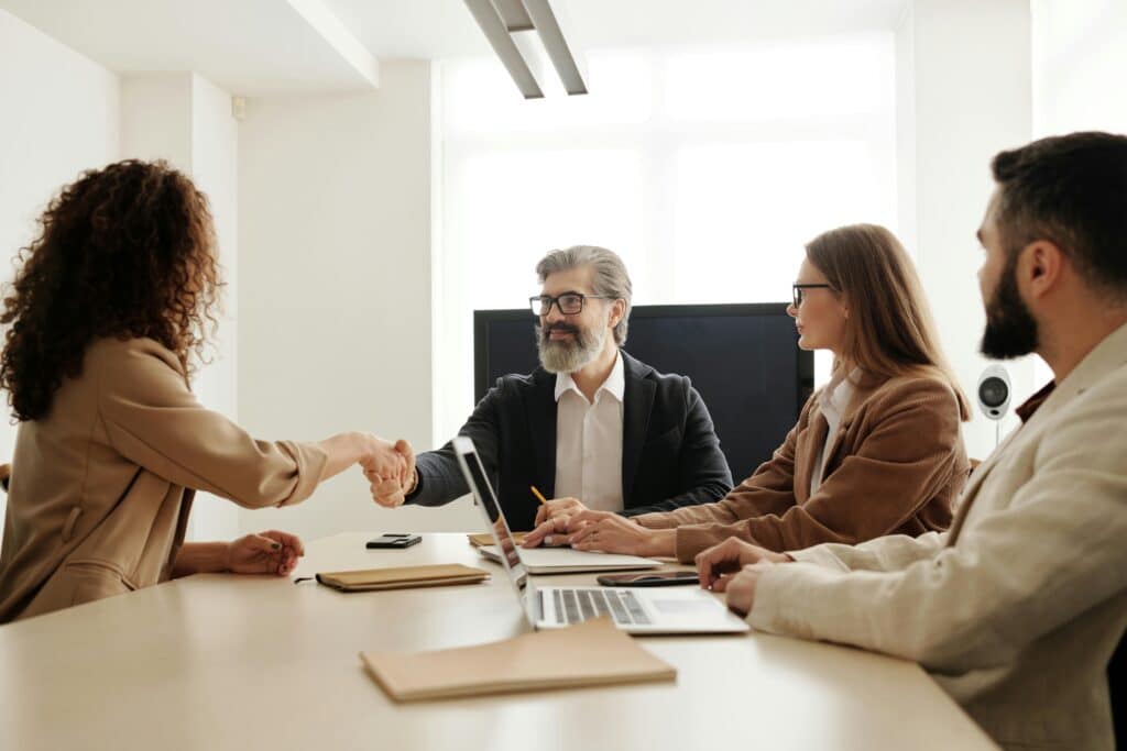 Während eines Meetings auf der Arbeit, schüttelt ein Mann einer Frau die Hand.